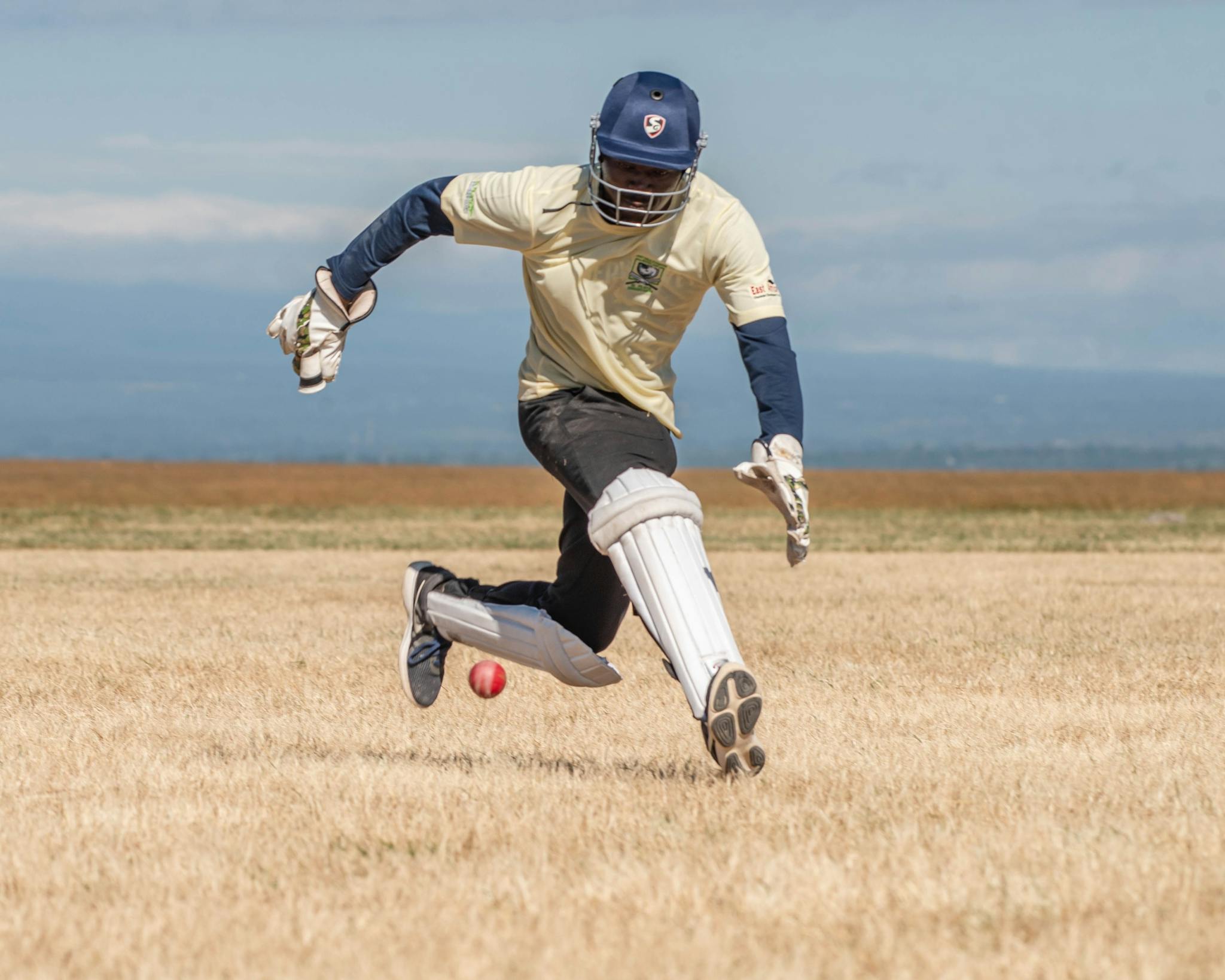 Cricketer skillfully fielding during an outdoor match on a sunny day.